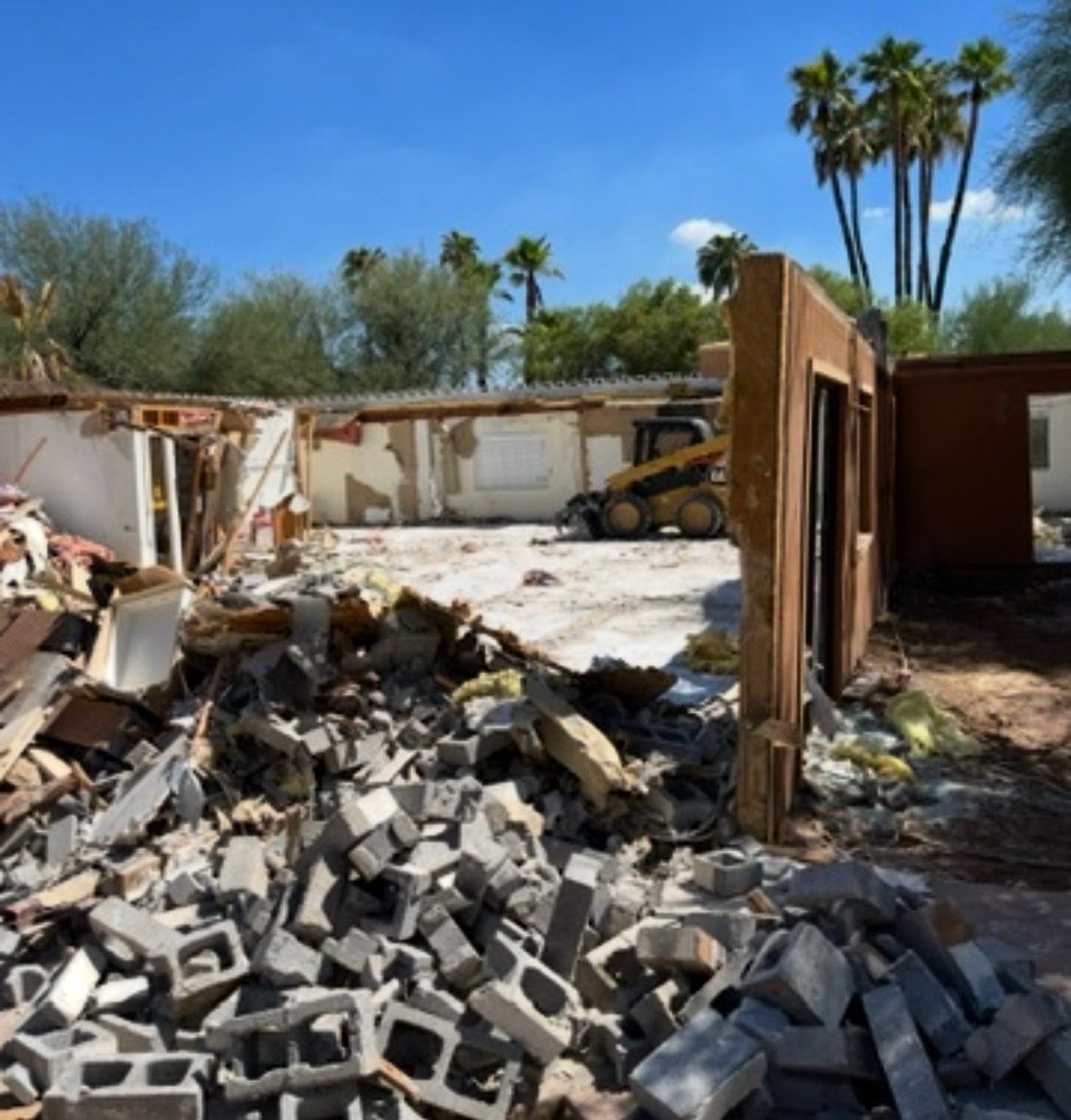Full house demolition in progress — block rubble pile and skid steer clearing the site in Phoenix