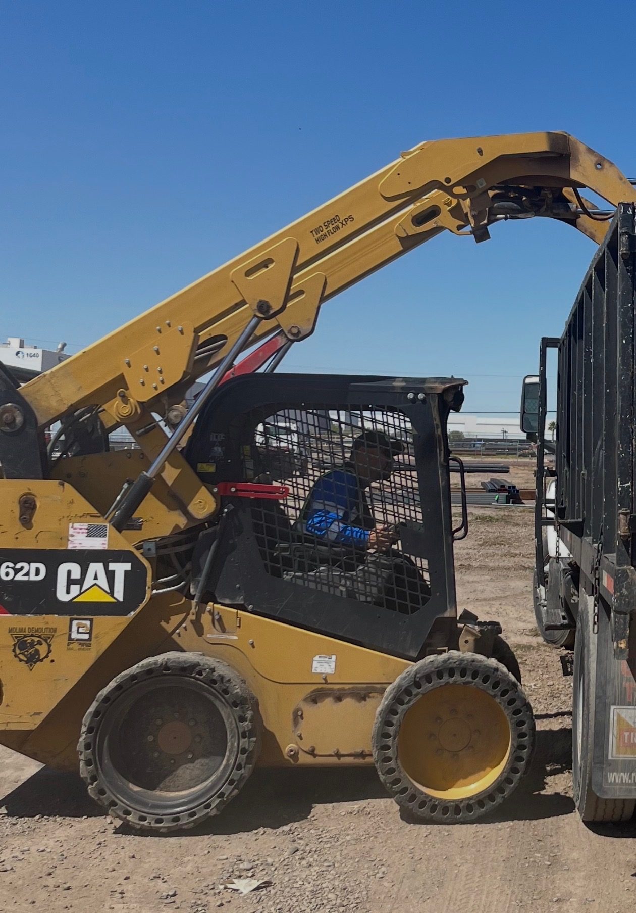 Molina Demolition branded CAT skid steer loading a dump truck on a job site